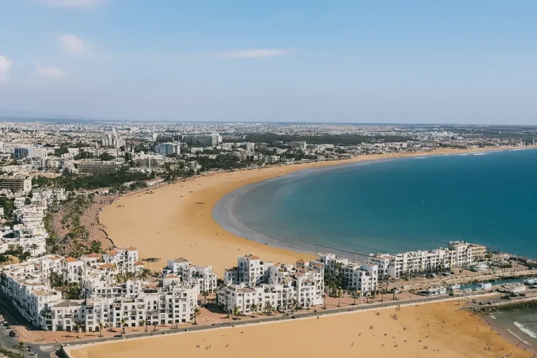 Panorama aérien d’Agadir illustrant un article sur le tourisme et les dangers potentiels en 2025, avec la plage, les immeubles blancs et l’océan Atlantique en arrière-plan.