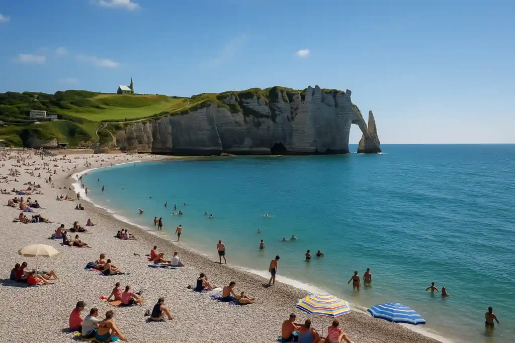 Falaises et plage de galets d’Étretat en Normandie, mer turquoise et ciel bleu, baigneurs et parasols colorés.