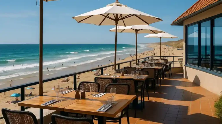 Terrasse de restaurant face à l’océan Atlantique à Biscarrosse-Plage, tables dressées et parasols, plage animée en arrière-plan.