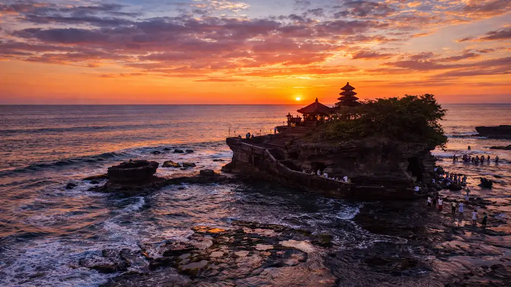 Temple Tanah Lot à Bali au coucher du soleil, perché sur un rocher en mer avec visiteurs à marée basse